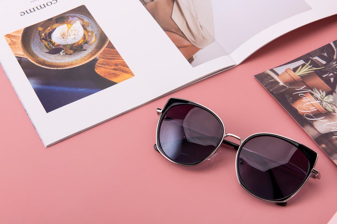 Fashion sunglasses placed on a pink surface with open magazines.